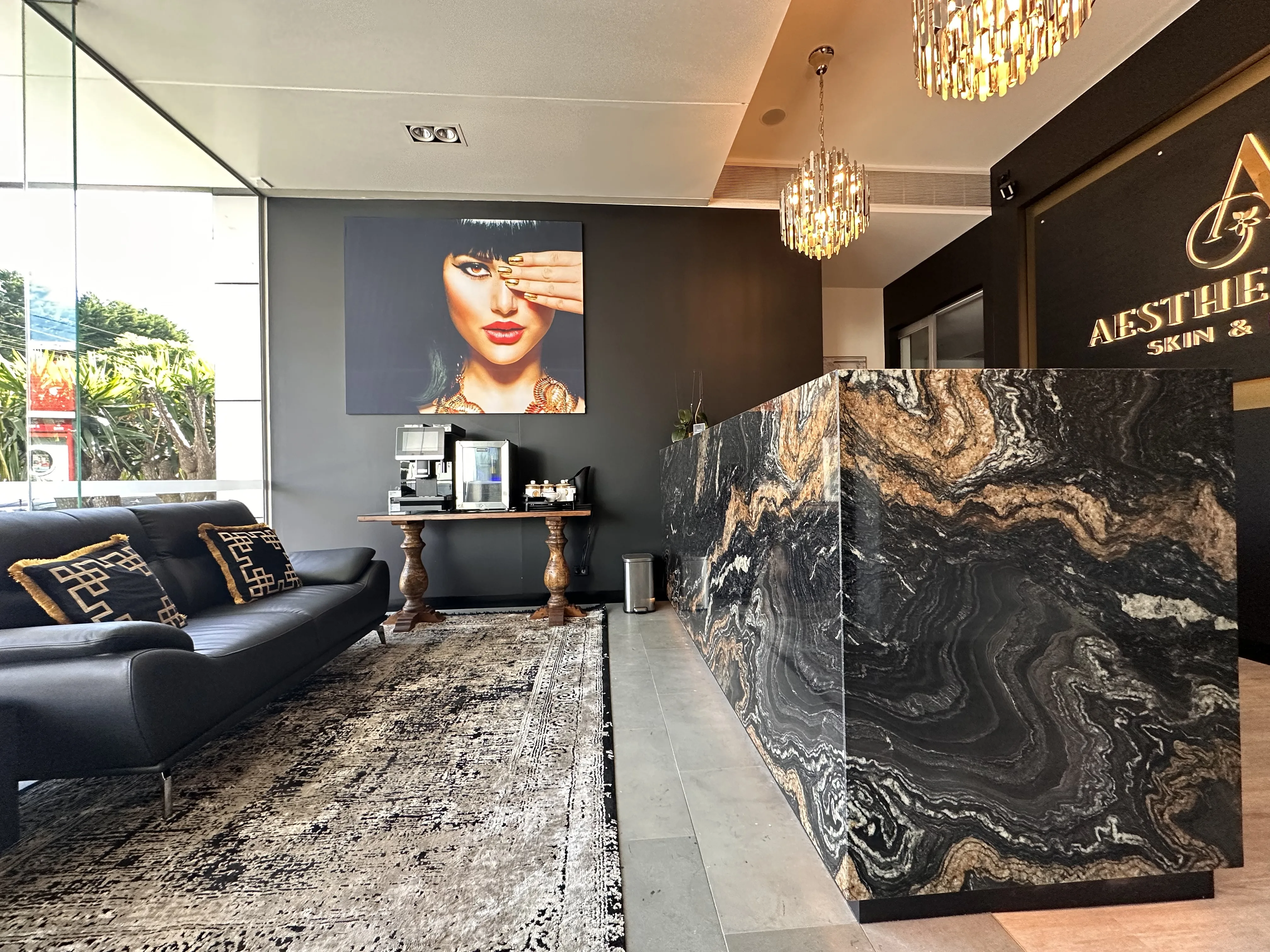 Aesthetique reception — black leather sofa, gold-fringe cushions, black and gold marble desk, crystal chandeliers