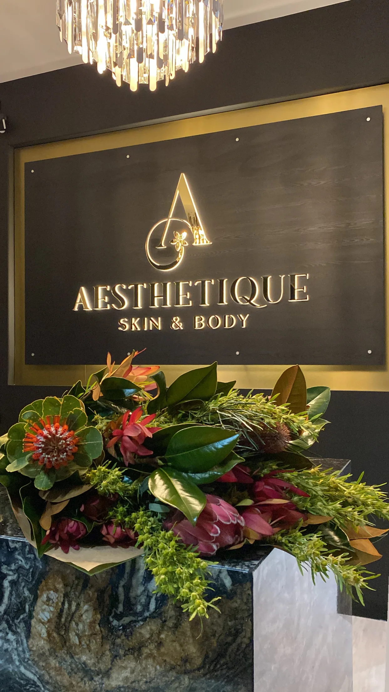 The Aesthetique Skin & Body gold monogram sign above a native floral arrangement at reception
