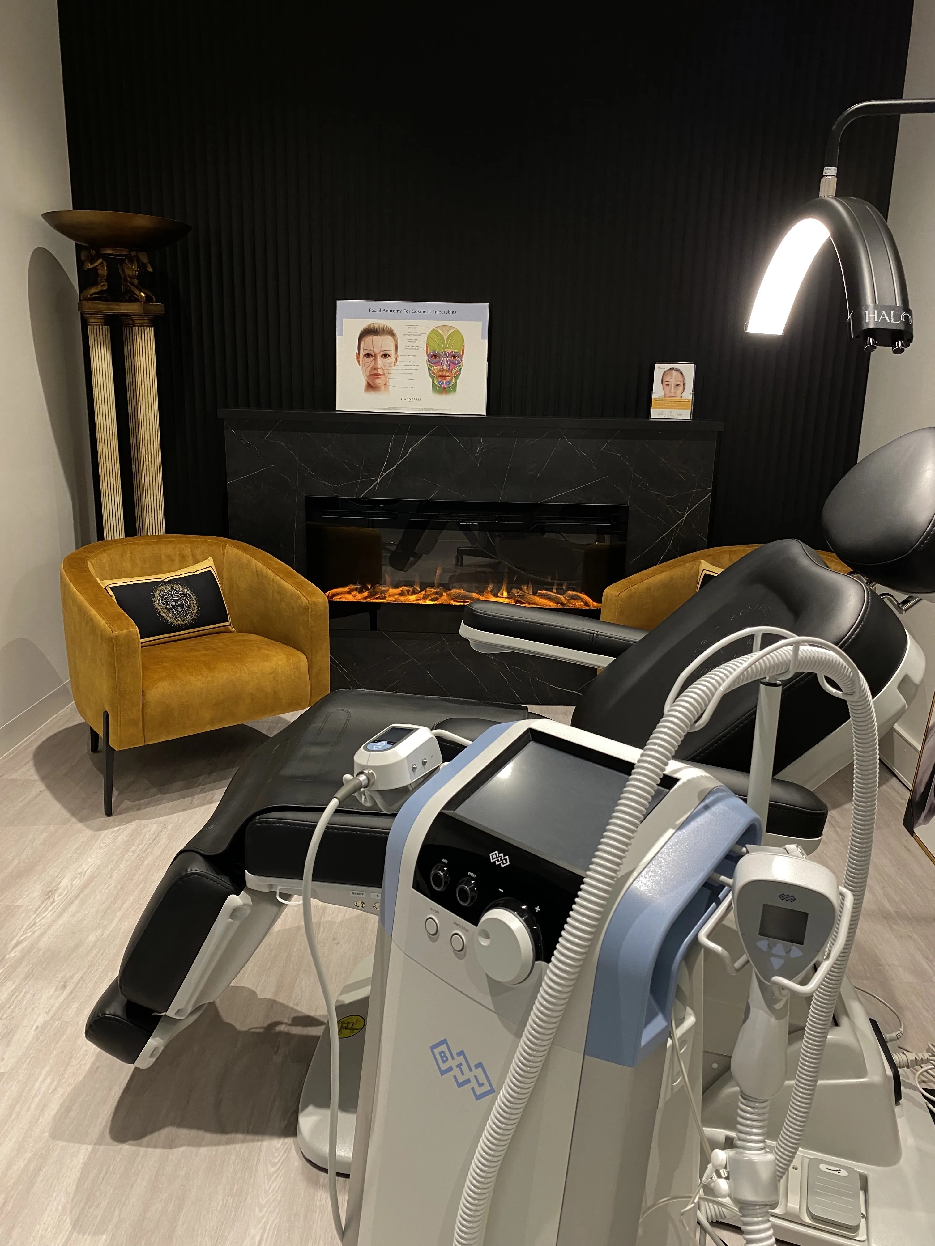 Treatment room with electric fireplace, mustard velvet armchair and Emsculpt device